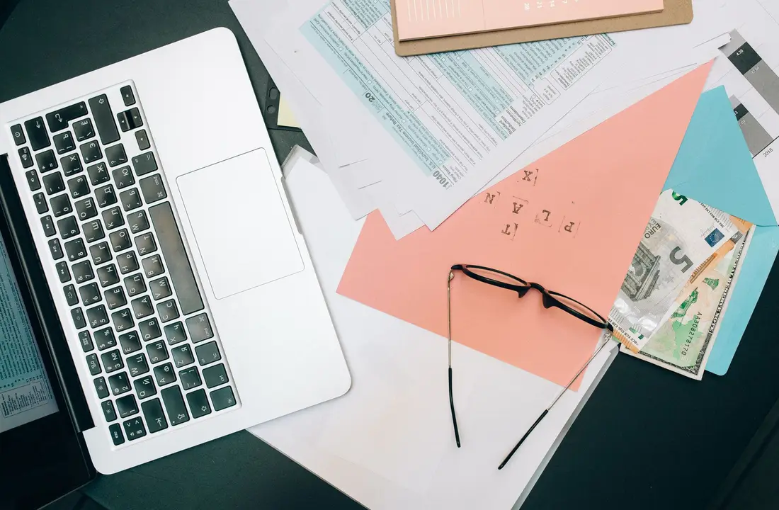 Un plan de travail rangé avec un ordinateur portable, des documents et des lunettes